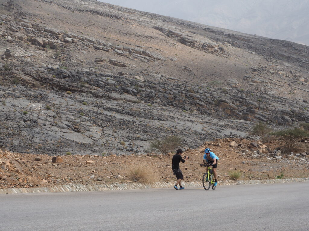 Video maker Pehuen Grotti on a desert road filming two cyclists.